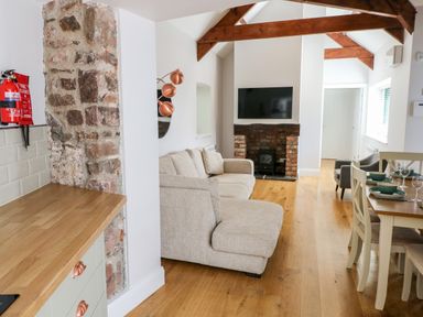 A living room with a beige sofa a wall-mounted TV and a dining table with chairs at Ramsey Cottage in Milford Haven