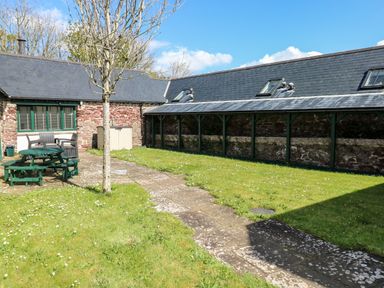 A garden with grass a tree a stone path and outdoor seating by stone buildings at Ramsey Cottage in Milford Haven