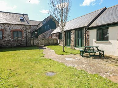 An outdoor area with stone buildings a paved pathway a tree and a green picnic table at Ramsey Cottage in Milford Haven