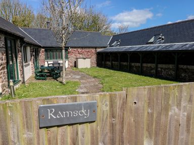 A fenced outdoor courtyard with a tree picnic table and two buildings with stone walls at Ramsey Cottage in Milford Haven
