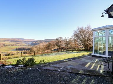 A backyard with a glass conservatory and bench overlooking fields and hills at Ty Twmp Tump Cottage in Tal-Y-Bont-On-Usk