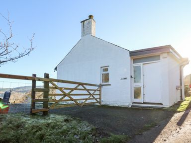A white cottage with a wooden gate and a dirt driveway at Ty Twmp Tump Cottage in Tal-Y-Bont-On-Usk
