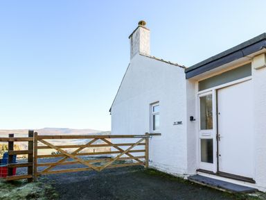 The exterior of a white cottage with a wooden gate and a view of hills at Ty Twmp Tump Cottage in Tal-Y-Bont-On-Usk