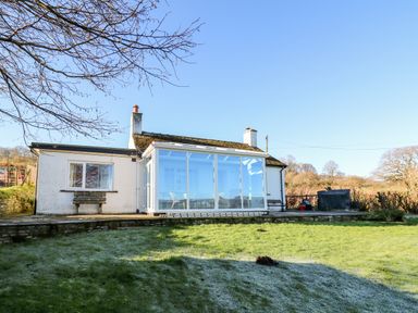 A white cottage with a glass sunroom and green lawn in front at Ty Twmp Tump Cottage in Tal-Y-Bont-On-Usk