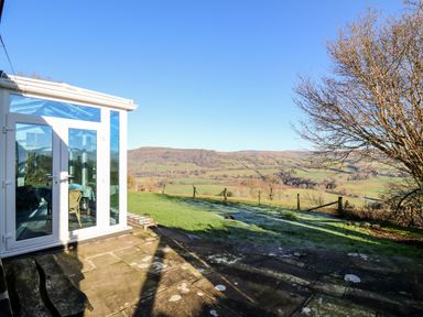A patio area next to a conservatory with a view of fields hills and a tree at Ty Twmp Tump Cottage in Tal-Y-Bont-On-Usk