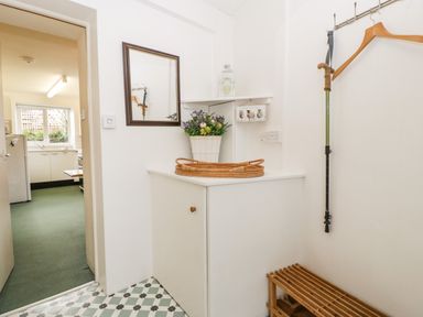 A small entryway with a cabinet holding a flower pot and a mirror on the wall a walking cane and coat hangers on the wall and a wooden bench below at Ty Twmp Tump Cottage in Tal-Y-Bont-On-Usk