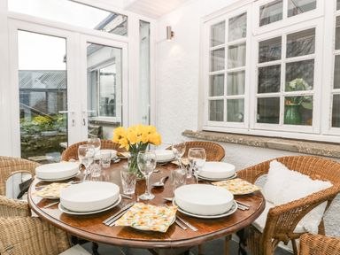 A dining area with a round wooden table set with bowls glasses and floral napkins surrounded by wicker chairs at Ty Twmp Tump Cottage in Tal Y Bont On Usk