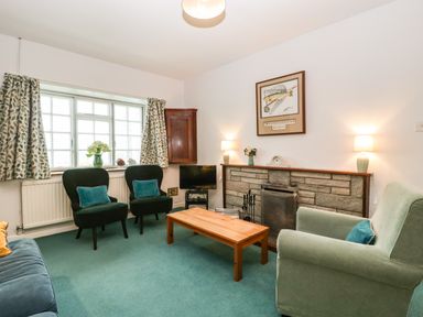 A living room with green carpet two armchairs a wooden coffee table and a fireplace at Ty Twmp Tump Cottage in Tal-Y-Bont-On-Usk