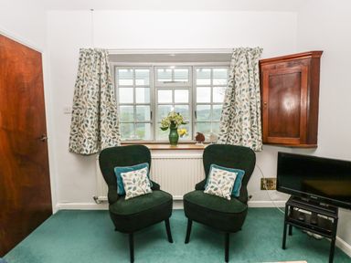 Two chairs with cushions in front of a window with floral curtains and a vase with flowers at Ty Twmp Tump Cottage in Tal-Y-Bont-On-Usk