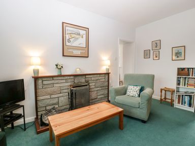 A sitting room with a fireplace television armchair coffee table and bookshelf at Ty Twmp Tump Cottage in Tal-Y-Bont-On-Usk