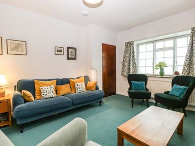 A living room with a blue sofa with cushions two black armchairs a wooden coffee table and framed pictures on the wall at Ty Twmp Tump Cottage in Tal-Y-Bont-On-Usk