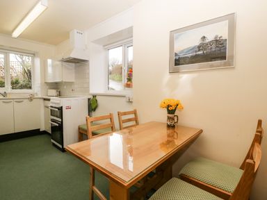 A kitchen with a wooden dining table and chairs a vase with flowers on the table a stove and cabinets with windows showing outside at Ty Twmp / Tump Cottage in Tal Y Bont On Usk