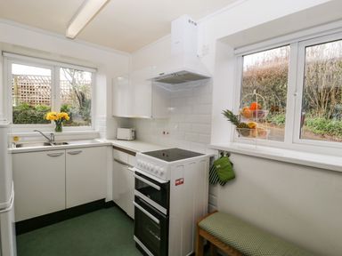 A kitchen with white cabinets a stove a double sink and windows showing garden at Ty Twmp Tump Cottage in Tal Y Bont On Usk