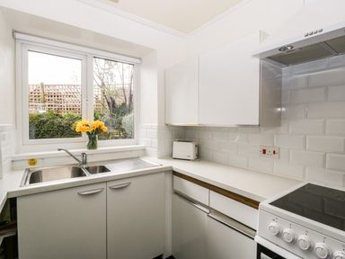 A kitchen with a double sink flowers on the windowsill a toaster white cabinets and an electric stove at Ty Twmp Tump Cottage in Tal-Y-Bont-On-Usk