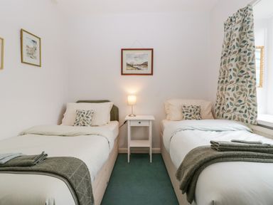 A bedroom with two single beds separated by a nightstand with a lamp and framed pictures on the walls at Ty Twmp Tump Cottage in Tal Y Bont On Usk