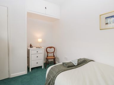 A bedroom with a single bed, a wooden chair, a white dresser with a lamp, and a framed picture on the wall at Ty Twmp Tump Cottage in Tal-Y-Bont-On-Usk