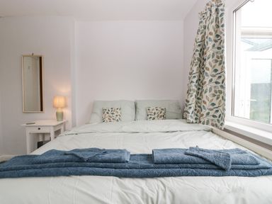 A bedroom with a double bed towels on bed a side table lamp and window with curtains at Ty Twmp Tump Cottage in Tal-Y-Bont-On-Usk