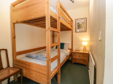 A small bedroom with wooden bunk beds a wooden nightstand with a lamp framed picture on the wall and a wooden chair at Ty Twmp Tump Cottage Tal-Y-Bont-On-Usk