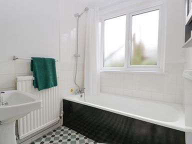 A bathroom with a bathtub, shower, window, sink, radiator with green towels, and tiled floor at Ty Twmp Tump Cottage in Tal-Y-Bont-On-Usk