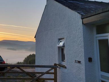 A white cottage wall with a small window and a gate with a car and misty hills at sunrise at Ty Twmp Tump Cottage in Tal-Y-Bont-On-Usk