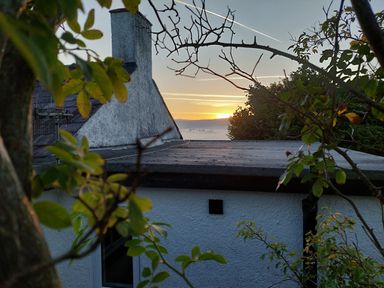 A view of a white house with a flat roof and chimney framed by tree branches at sunset at Ty Twmp Tump Cottage in Tal Y Bont On Usk