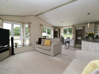 A living room with two beige sofas a dining table and chairs and a kitchen area at Hill View Lilac Lodge in Wareham