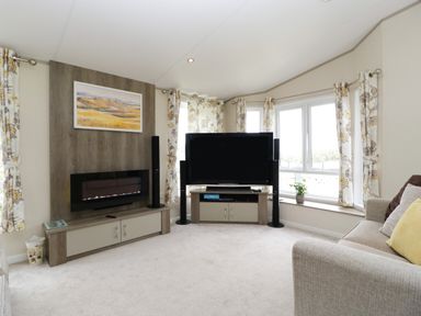 A living room with a sofa television speakers fireplace and windows with floral curtains at Hill View Lilac Lodge in Wareham