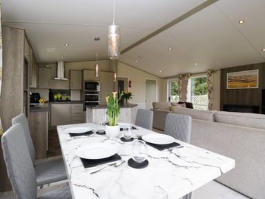 A dining table set with plates and glasses in an open kitchen and living room area at Hill View Lilac Lodge in Wareham