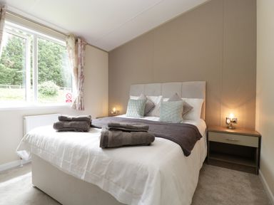 A bedroom with a double bed pillows folded towels bedside tables and a window with floral curtains at Hill View Lilac Lodge in Wareham
