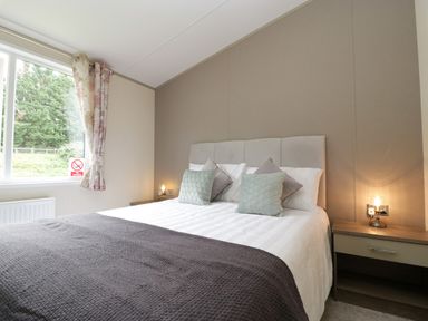 A bedroom with a double bed bedside tables and a window with floral curtains at Hill View Lilac Lodge in Wareham