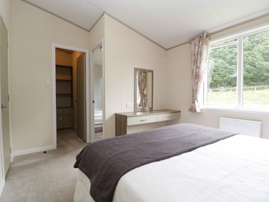 A bedroom with a bed gray blanket wall mirror and dresser next to a window with floral curtains at Hill View Lilac Lodge in Wareham