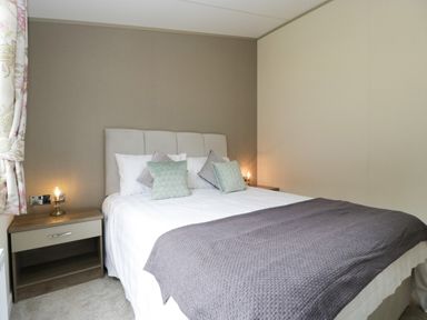 A bedroom with a bed with pillows and a blanket with bedside tables and lamps at Hill View Lilac Lodge in Wareham