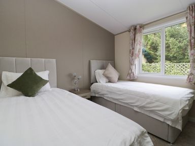 A bedroom with two single beds with pillows and a window with floral curtains at Hill View Lilac Lodge in Wareham