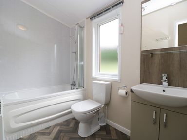 A bathroom with a bathtub shower combination a toilet a sink with cabinet and a window at Hill View Lilac Lodge in Wareham