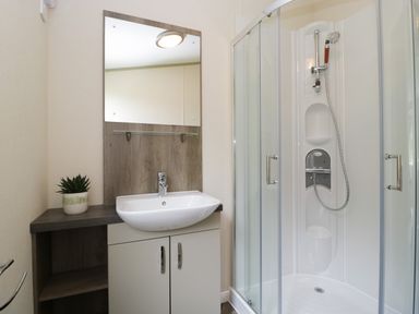A bathroom with a sink and mirror next to a glass shower enclosure at Hill View Lilac Lodge in Wareham