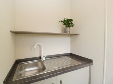 A kitchen sink with a white faucet and a wooden shelf above with a potted plant at Hill View Lilac Lodge in Wareham