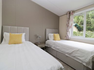 A bedroom with two single beds a nightstand and a window at Hill View Lilac Lodge in Wareham