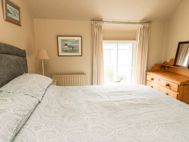 A bedroom with a bed a wooden dresser a table lamp and framed pictures on the walls at Silva in Penmon