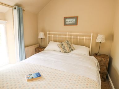 A bedroom with a double bed bedside tables with lamps a window with blue curtains and a book on the bed at Silva in Penmon
