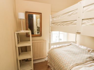 A small bedroom with a white bunk bed a wooden shelf with a lamp and a wall mirror at Silva in Penmon