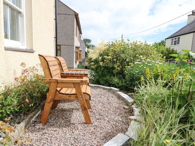 A garden with two wooden chairs on a gravel path next to flowering plants at Silva in Penmon