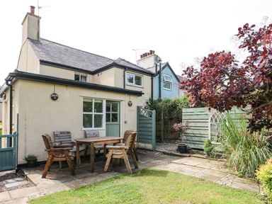 An outdoor patio with a wooden table and chairs near a light yellow house with a green door and windows at Silva in Penmon