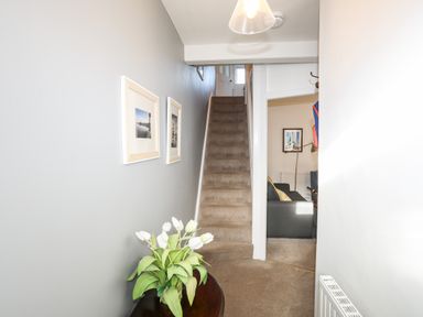 A hallway with carpeted stairs and framed pictures on the wall with a table holding white flowers by Silva in Penmon