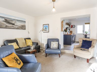 A living room with blue and beige armchairs a dark grey sofa with yellow pillows a small wooden coffee table and a view into a kitchen at Silva in Penmon