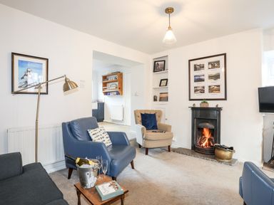 A living room with blue and beige armchairs a fireplace and framed pictures at Silva in Penmon