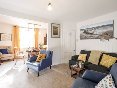 A living room and dining area with blue and beige chairs and yellow cushions at Silva in Penmon