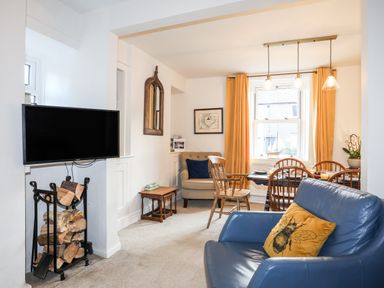 A living room with a blue armchair and yellow pillow near a dining table with four wooden chairs at Silva in Penmon