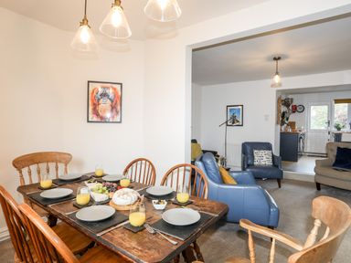 A dining table set with plates and glasses of juice next to a living area with armchairs and a sofa at Silva in Penmon