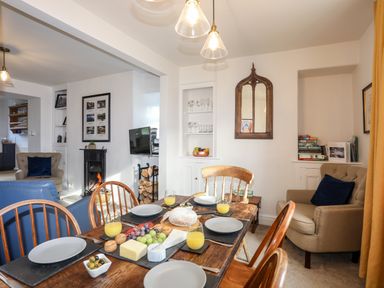 A dining room with wooden table set with plates and juice glasses and a living area with chairs and a fireplace at Silva in Penmon