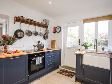 A kitchen with pots hanging on a rack a stove a sink and a door with windows at Silva in Penmon